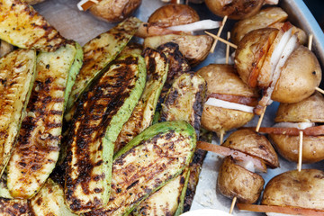 close-up appetizing slices of courgettes and potatoes with bacon roasted on a grill