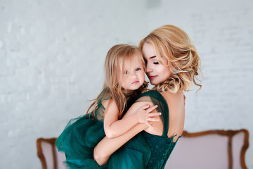 Portrait of a beautiful young mother with a cute blonde daughter sitting in white interior dressed...