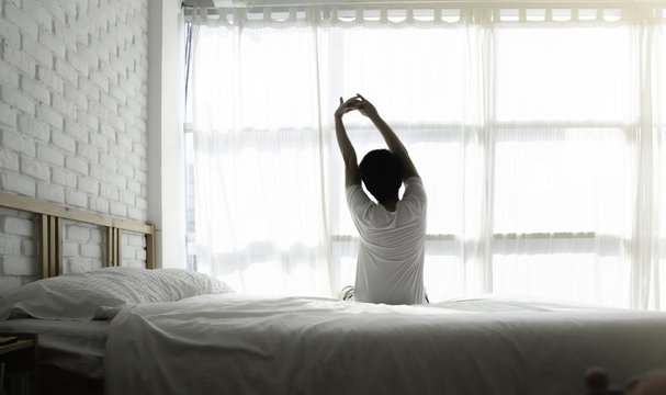 Men sit at the edge of the bed. And stretching his arms to relax in the morning.Wake up in the morning.Stretching after waking.