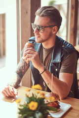 Hipster with a stylish haircut and beard sits at a table, stopped to lunch at a roadside cafe.
