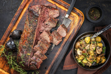 Traditional barbecue aged marinated saddle of venison with fried potatoes and mushroom as top view on a cutting board