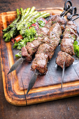Traditioneller russischer Schaschlik Lamm Grillspieß mit grünen Spargel und Paprika als closeup auf verbrannten Schneidebrett