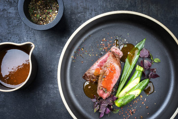 Modern barbecue dry aged sliced fillet steak with wild garlic and baby zucchini as top view on a plate with hot spices and sea buckthorn sauce