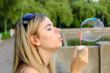 Attractive young woman enjoying in the park blowing soap bubbles