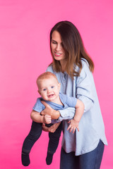 family, motherhood, parenting, people and child care concept - happy mother holds adorable baby over pink background