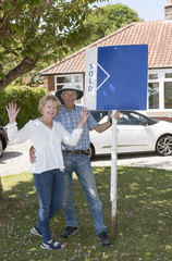 Couple standing with a sold sign outside their home