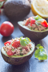 Salad with tuna, avocado, tomatos, coriander and lemon juice served in avocado bowl, ingredients on background, vertical