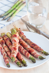 Healthy appetizer, green asparagus wrapped with bacon on a white plate, vertical