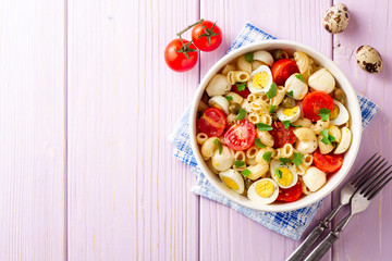 Pasta salad with quail eggs, mozzarella, cherry tomatoes and capers in bowl on purple wooden background