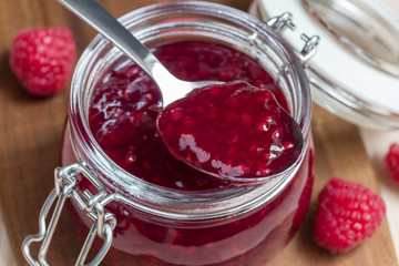 Raspberry jam in glass jar on a wooden board, horizontal
