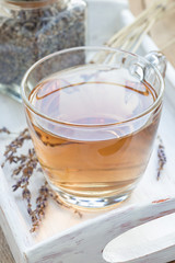 Herbal lavender tea in glass cup with lavender flowers on a wooden tray, vertical