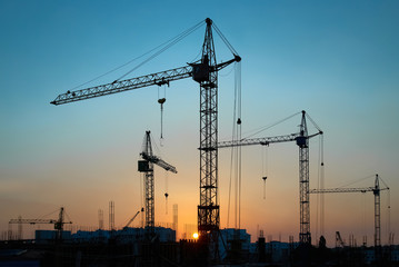 Industrial landscape with silhouettes of constraction cranes on dramatic sunset background