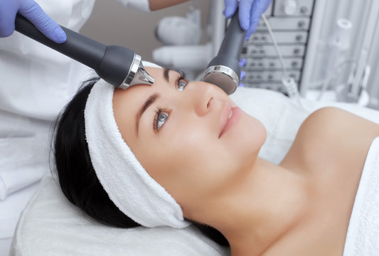 The cosmetologist makes the procedure an ultrasonic cleaning of the facial skin of a beautiful, young woman in a beauty salon.Cosmetology and professional skin care.