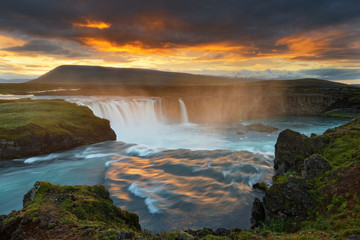 Fototapeta na wymiar Scenic view of a waterfall in a wide sunset landscape, the colorful light reflected in the water, dark clouds above the scene - Location: Iceland, Godafoss (Goðafoss)