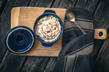 Barley porridge in the blue ceramic pot on dark aged wooden background. Healthy breakfast.