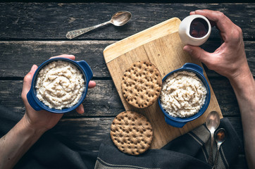 Barley porridge with strawberry jam in the blue ceramic pot and bread on dark aged wooden background. Healthy breakfast. Man pours porridge with jam.