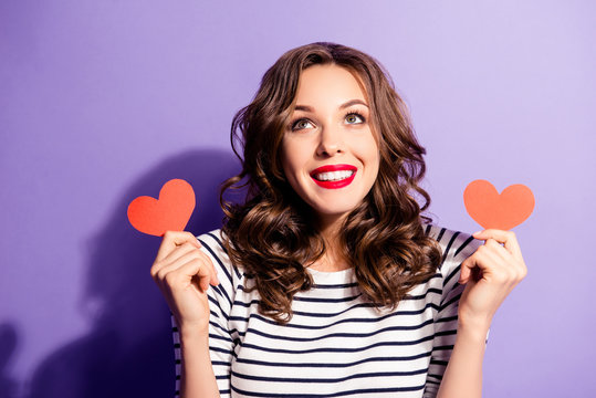 Portrait of thoughtful ponder girl in good mood having two little small red paper carton hearts in hands looking up isolated on violet background