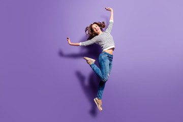 Portrait of cheerful positive girl jumping in the air with raised hands and leg looking at camera...