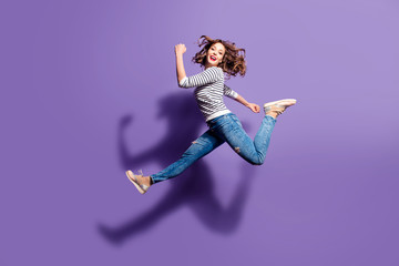 Fototapeta Portrait of sportive active girl in motion jumping over in the air isolated on violet background having perfect stretching looking at camera obraz