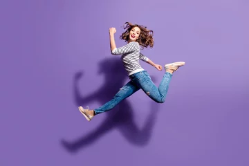 Foto op Plexiglas Portrait of sportive active girl in motion jumping over in the air isolated on violet background having perfect stretching looking at camera © deagreez