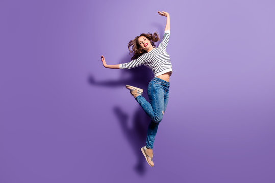Portrait of cheerful positive girl jumping in the air with raised hands and leg looking at camera isolated on violet background. Life lifestyle energy people concept