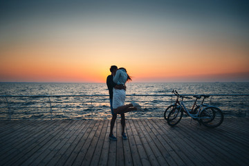 Fototapeta premium Couple of young hipster lovers kissing at the beach at sunrise sky at wooden deck summer time