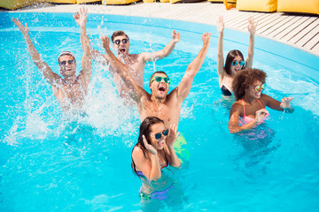 Funky mood non stop. Six excited international tourists are enjoying at the sea side, guys jump and dabble ladies scream and laugh, raised up arms, dancing all day long, aclive time on resort