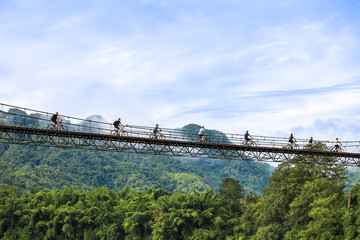 Obraz premium Tourists riding on bicycle across suspension bridge in Kanchanaburi, Thailand
