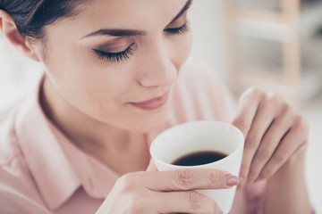 Head close up shot high angle view of attractive pleasant charming woman with long nature eyelashes keeping her eyes closed while smelling aromatic coffee, morning energy, people concept