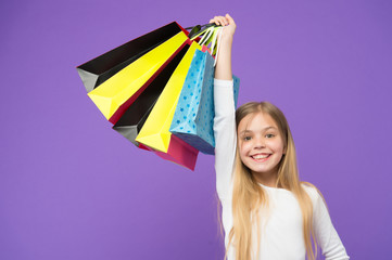 Happy child with paper bags. Little girl smile with shopping bags on violet background. Kid shopper...