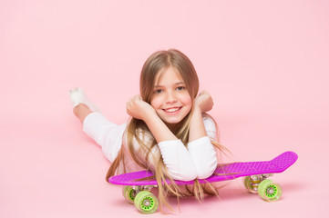 Obraz na płótnie Canvas Small girl smile with skate board on pink background. Child skater smiling with longboard. Skateboard kid lie on floor. Childhood lifestyle and active games. Sport activity and energy, punchy pastel