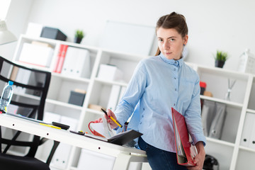 A young girl in the office is standing, leaning on a table, and writing in a diary.