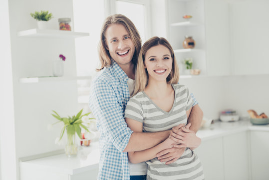 He vs she together forever! Portrait of positive toothy partners embracing in modern white kitchen with interior looking at camera. Daydream delight mood concept