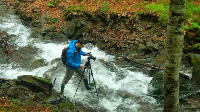 traveler photographer shoots beautiful sunset on the shore of a mountain river