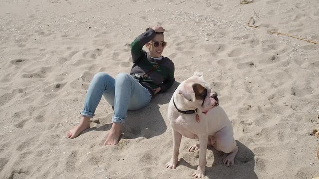 Slow motion of a cute caucasian woman and her white boxer dog relaxing on the beach