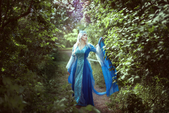 Young woman elf in a blue dress standing in a fairy forest.