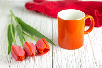 Three red tulips and a red cup, a white wooden table.