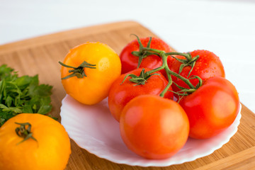Fresh red and yellow tomatoes close up on a wooden board at a white textured table