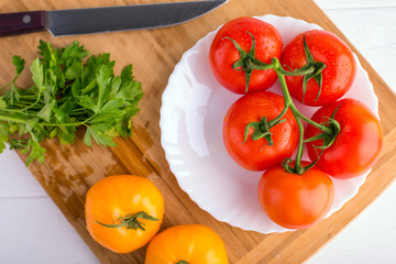 Fresh red and yellow tomatoes from above on a wooden board with a knife in a white plate at a white textured table