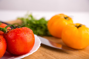 Fresh red and yellow tomatoes close up on a wooden board with a knife at a white textured table