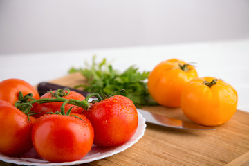 Fresh red and yellow tomatoes close up on a wooden board with a knife at a white textured table