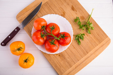 Fresh red and yellow tomatoes from above on a white plate on a wooden board with a knife