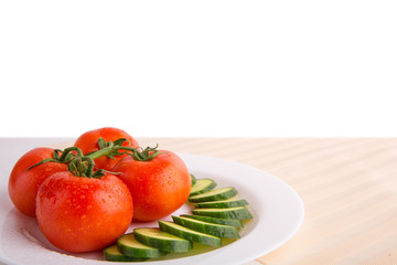 Fresh red tomatoes with sliced cucumber on a white plate isloated with copy space