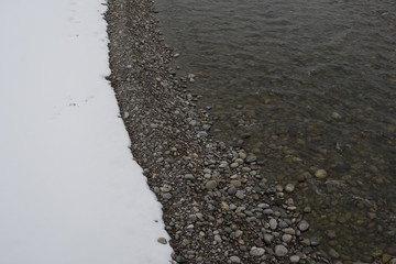 close up rock pebbles on the river bank with white snow on the ground