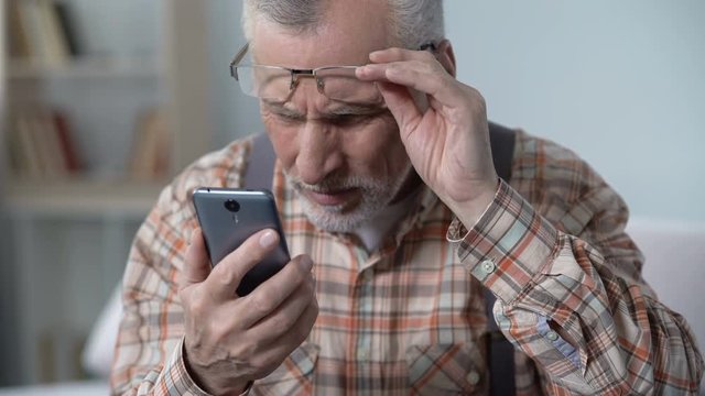 Old man looks incredulously at cellphone, new technology complicated for elderly