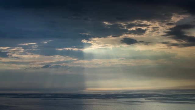timelapse shot of beautiful moody stormy sky with clouds hiding the sun and reflection in the sea below