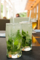 Two glasses with gin and tonic served with ice and lime on a wooden table.