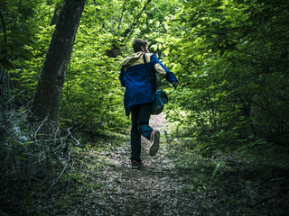 young scary man running away in the dark forest on the path back view