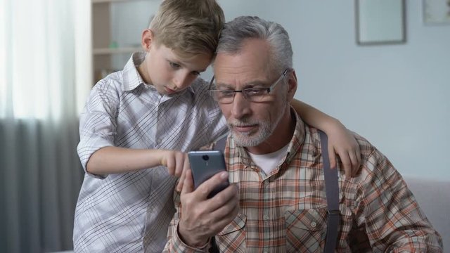 Grandson explaining grandpa how to use smartphone, boy feels to be important