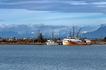 Fototapeta premium Fishing boats at the Marina near the village at the background of mountain range and cloudy sky